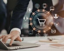 Osoba pracująca na laptopie z graficznym symbolem koszyka i ikonami kanałów digital wokół – koncepcja rozwoju e-commerce i sprzedaży wielokanałowej.